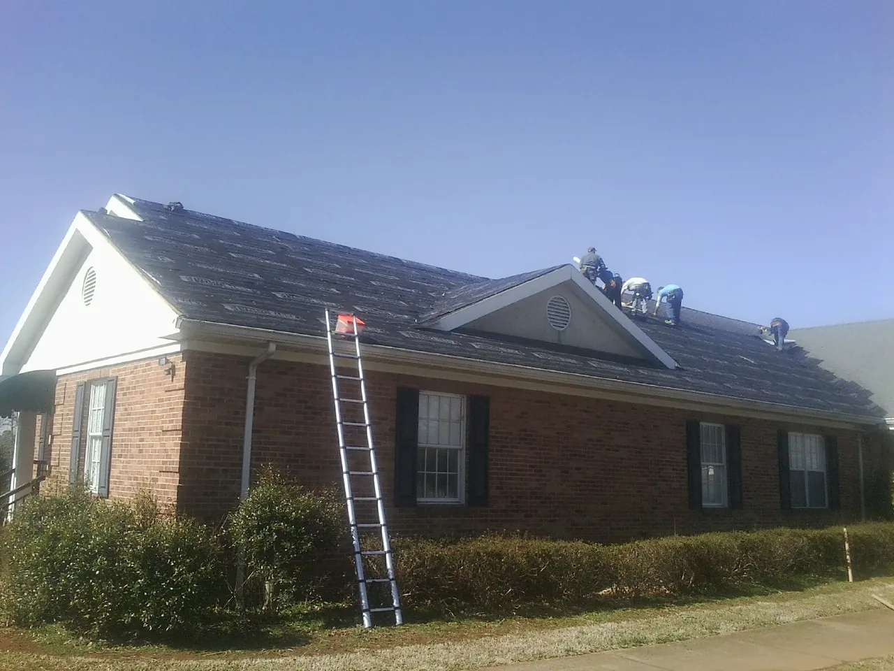 Crew tearing shingles off a brick ranch roof with a ladder set — Metal Roof Repair work by our crew in Townville